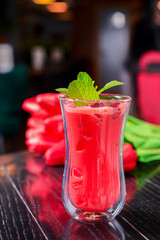 Red alcohol raspberry cocktail served in a unique design glass with a bouquet of red tulips on the background.