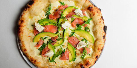 Delicious pizza with salmon, cheese, avocado and fresh arugula. Over white background.
