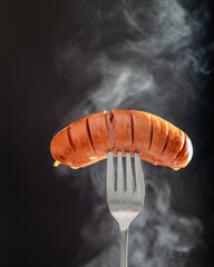 Grilled sausage. Close-up. Grilled sausage on a fork isolated on black background, steam from...
