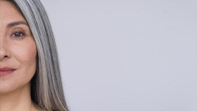 Senior older middle aged Asian woman with grey hair and radiant face with perfect skin. Advertising of rejuvenating skincare and makeup for natural radiant healthy skin. Closeup cut. Copy space.