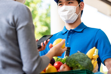 Fototapeta premium Hygienic Asian deliveryman wearing face mask while delivering groceries to customer at home, food delivery in the time of pandemic concept