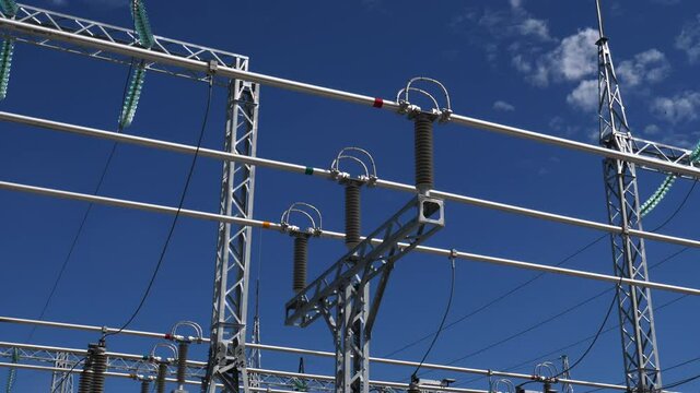 Power transmission lines with metal supports and insulators at modern electrical distribution substation against blue sky