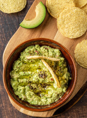 Bowl of guacamole with tortilla chips on wooden background