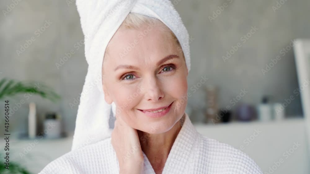 Canvas Prints Happy smiling attractive middle aged woman wearing bathrobe and white towel touching face looking at camera. Advertising of skin care spa procedures concept. Closeup portrait.