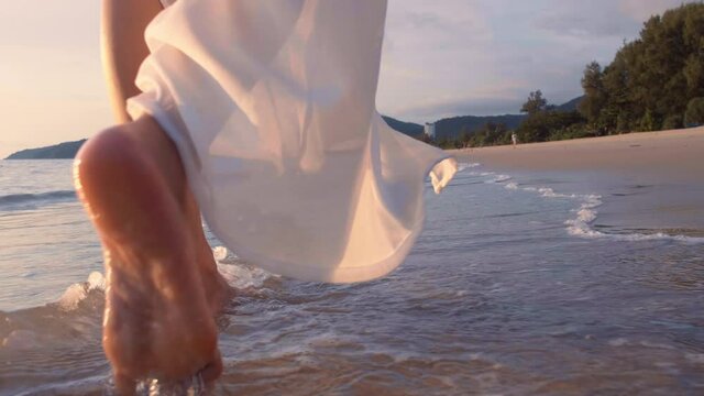 4K Slow motion woman feet walking barefoot on the beach at golden sunset time. leaving footprints in sand. Female tourist on summer vacation holiday relax at tropical beach Phuket, Thailand.