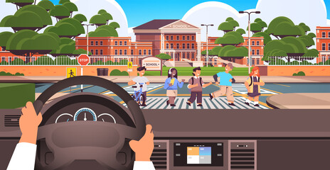 driver holding the steering wheel and waiting schoolchildren crossing road on crosswalk near school building road safety