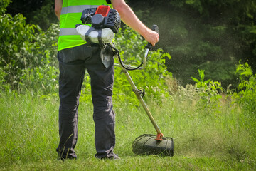 Worker mowing grass with grass trimmer