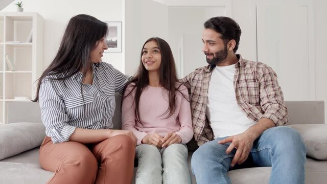 Happy family portrait. Parents listening to child daughter talking to them. Smiling laughing mom, dad and teenage kid having fun enjoying spending leisure time together at home sitting on sofa.