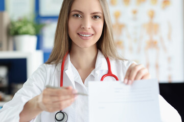 Smiling female doctor holding prescription blank for medicines