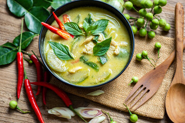 Chicken green curry Thai food on soup bowl with ingredient vegetable herbs and spices pepper chili on wooden table background, Traditional green curry chicken cuisine asian food. Top view