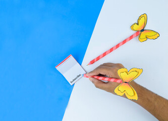Person writing on a small miniature little hand made diary placed on a blue paper background