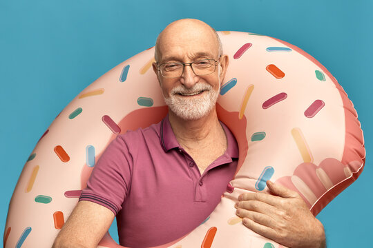 Vacations, summertime and relaxation. Studio image of cheerful charismatic old man wearing eyeglasses and t-shirt relaxing on summer hot day, going to swimming pool, holding inflatable ring