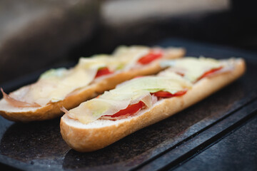 Grilled baguette smeared with butter and oil, chicken ham, tomato and covered with sliced cheese is baked until golden brown on a granite stone placed on the hearth