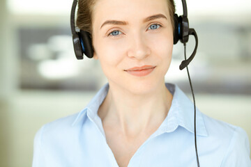 Beautiful female specialist with headphones helping customers online and smiling charmingly in modern call center office. Business people concept