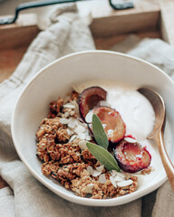 Granola with roasted plums and sage leaves on wooden tray with linen napkin