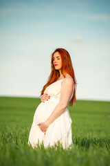 Fototapeta na wymiar Pregnant woman on the summer green field wearing long white dress