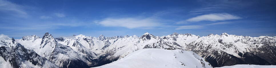 Fototapeta na wymiar Panorama of high snow-capped mountain peaks and beautiful blue sky with clouds at sunny day