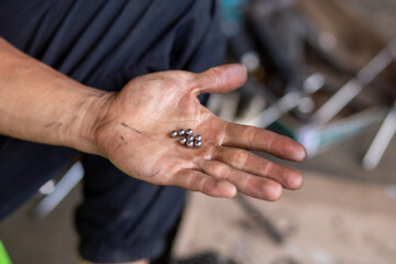 A small iron ball by a mechanic's hand. hands are stained with oil. Bicycle bearing The hand of a motorcycle mechanic in Thailand
