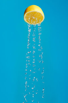 Lemon as a metaphor for a shower isolated on a blue background. Creative fruit food or drink concept. Lemon juice as a favorite summer refreshing drink with rain, splash and drops.