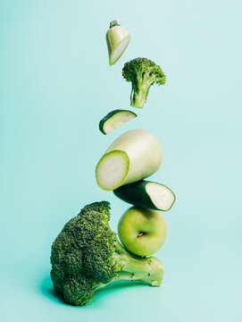 Naklejki Cut broccoli and zucchini with green apple isolated on a light blue background. Fresh and healthy ingredients for a vegan diet. Salad with veggies falling down. Creative food concept.