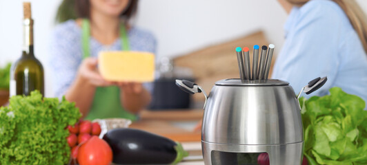 Fondue in a pot at the background of friends cooking together, close-up. Kitchen interiors and cookware