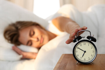 Sleepy young woman stretching hand to ringing alarm willing turn it off. Early wake up, not getting...
