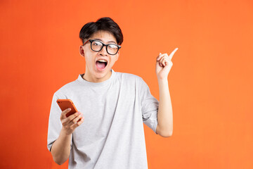 Portrait of young asian man holding smartphone in hand and pointing, isolated on orange background
