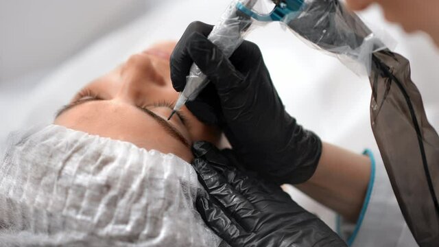 Closeup female cosmetologist hands in gloves correcting shape of brows to client at sterile salon
