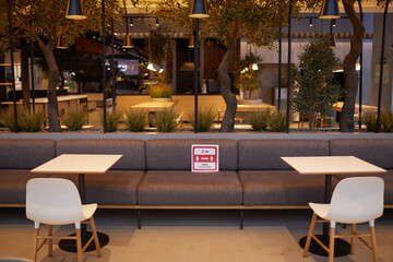 Wide angle background image of empty food court interior at shopping mall with red social distancing sign between tables, copy space