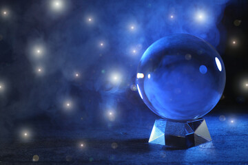 Magic crystal ball on table and smoke against dark background, space for text. Making predictions