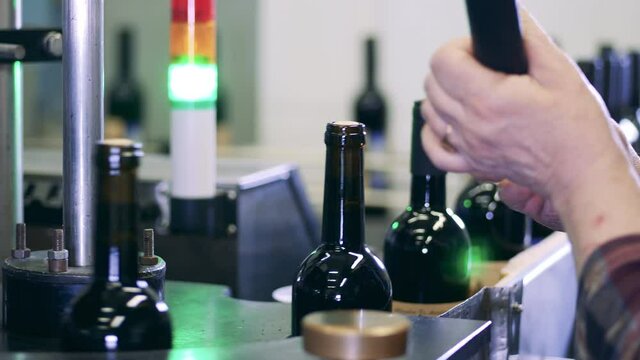 Workers fitting caps onto bottles of wine at a factory