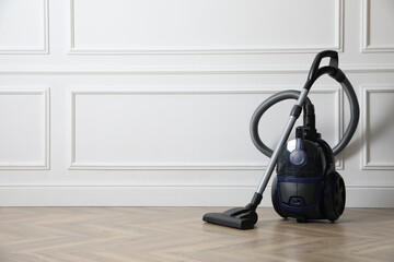 Modern vacuum cleaner near white wall indoors, space for text