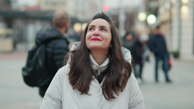 Portrait Attractive young woman face close up smiling looks up rejoices on walk slow motion along city streets in winter. Positive emotions. Travel tourism. Lifestyle freedom Relax