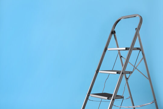 Metal stepladder on light blue background, space for text. Construction equipment