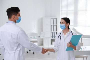 Doctors with protective masks giving handshake in clinic - Powered by Adobe