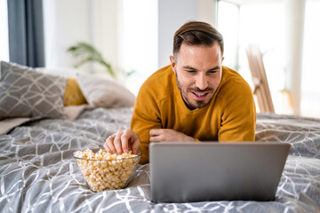 Man watching a laptop computer, lying on the bed at home.