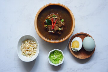 a bowl of black beef soup and the ingredient in white background 
