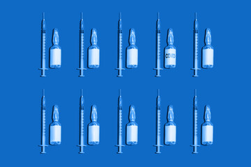 Fototapeta premium Single-use syringes and canisters with coronavirus vaccine on a blue background with space on the labels for copying.