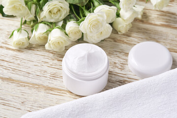 Obraz na płótnie Canvas Natural face cream or lotion, organic cosmetic to moisturize the skin with towel and white roses in the background.Top view.