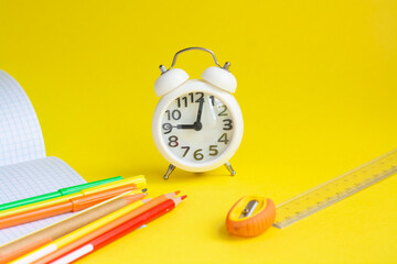 School, alarm clock, pencils, markers, notebook, pen, ruler and sharpener on a yellow background