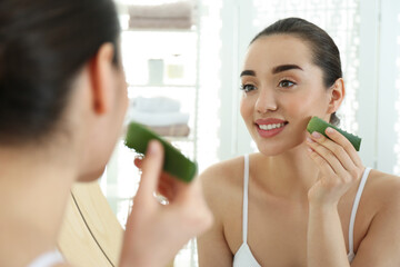 Young woman with aloe vera leaf near mirror indoors