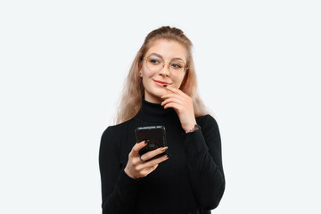 Fototapeta premium Image of a thoughtful young beautiful woman in casual clothes holding her smart phone. White background