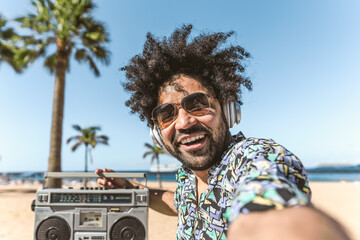 Young Latin man having fun taking selfie with mobile smartphone while listening music with...