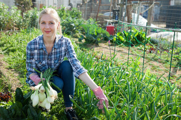 Portrait of teen girl gardener picking harvest of onion in sunny garden