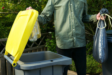 Person performing a selective sorting of household waste in recycling bins. Man putting plastic...