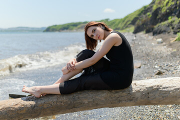 Young woman in black dress sitting on sand and enjoys sea.