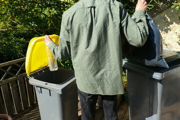 Person performing a selective sorting of household waste in recycling bins. Man putting plastic...