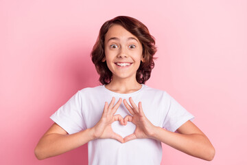 Photo of amazed cheerful little boy make fingers heart shape affection isolated on pastel pink color background