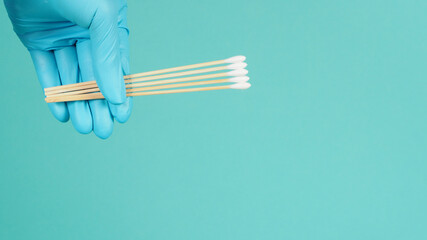 Cotton sticks for swab in hand with blue medical gloves or latex glove on mint green or Tiffany...