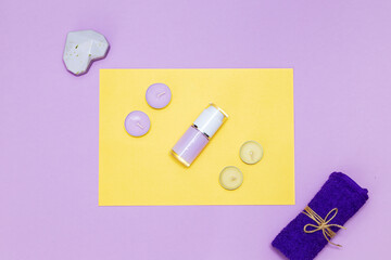 Scented candles, towel and lotion on a yellow and purple background.